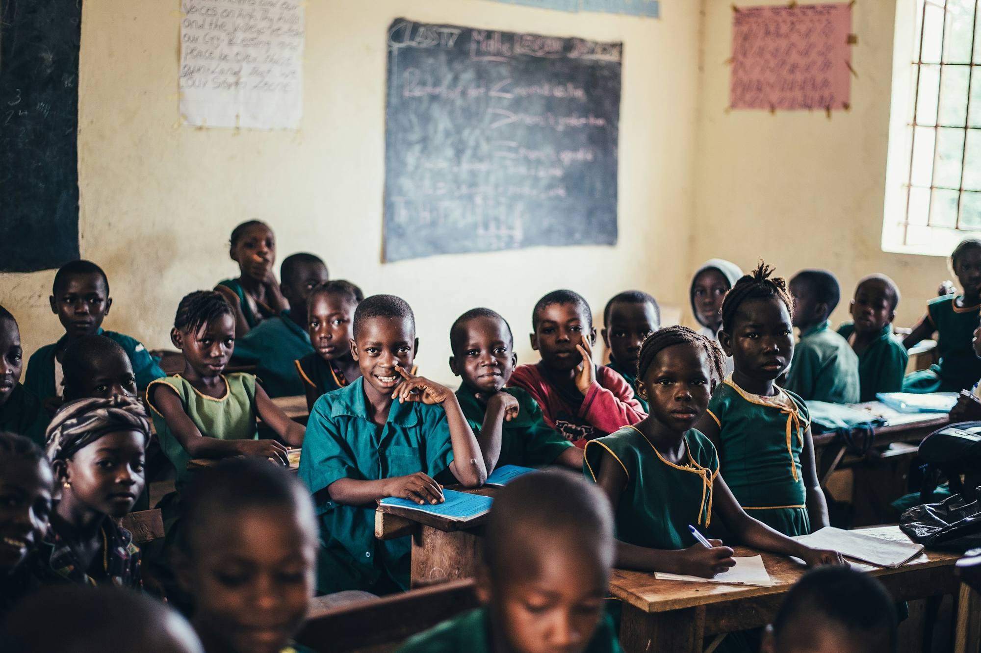 A classroom of Nigerian primary school students in green uniforms, many looking towards the camera