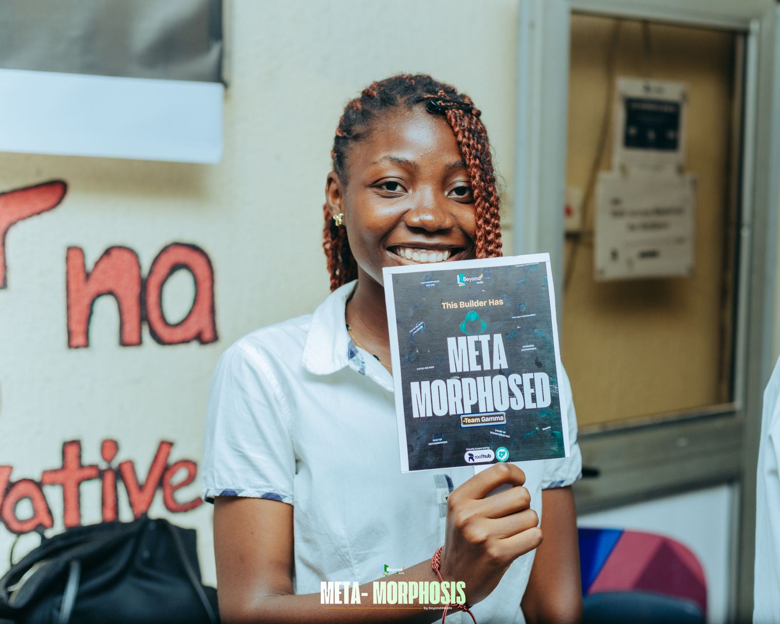 A smiling attendee holds up a card that reads "Meta Morphosed"