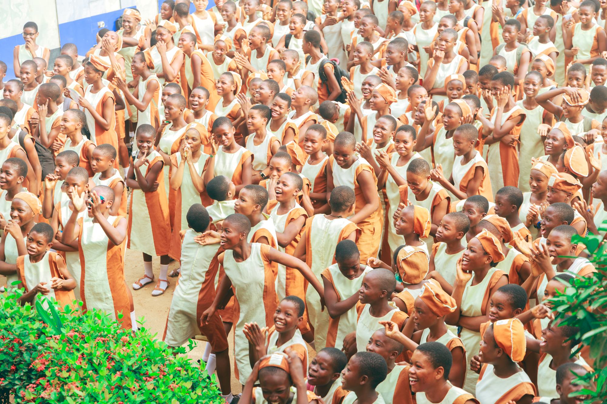 A crowd of secondary school students in orange and cream uniforms cheering with their arms raised during the Discovering Me outreach