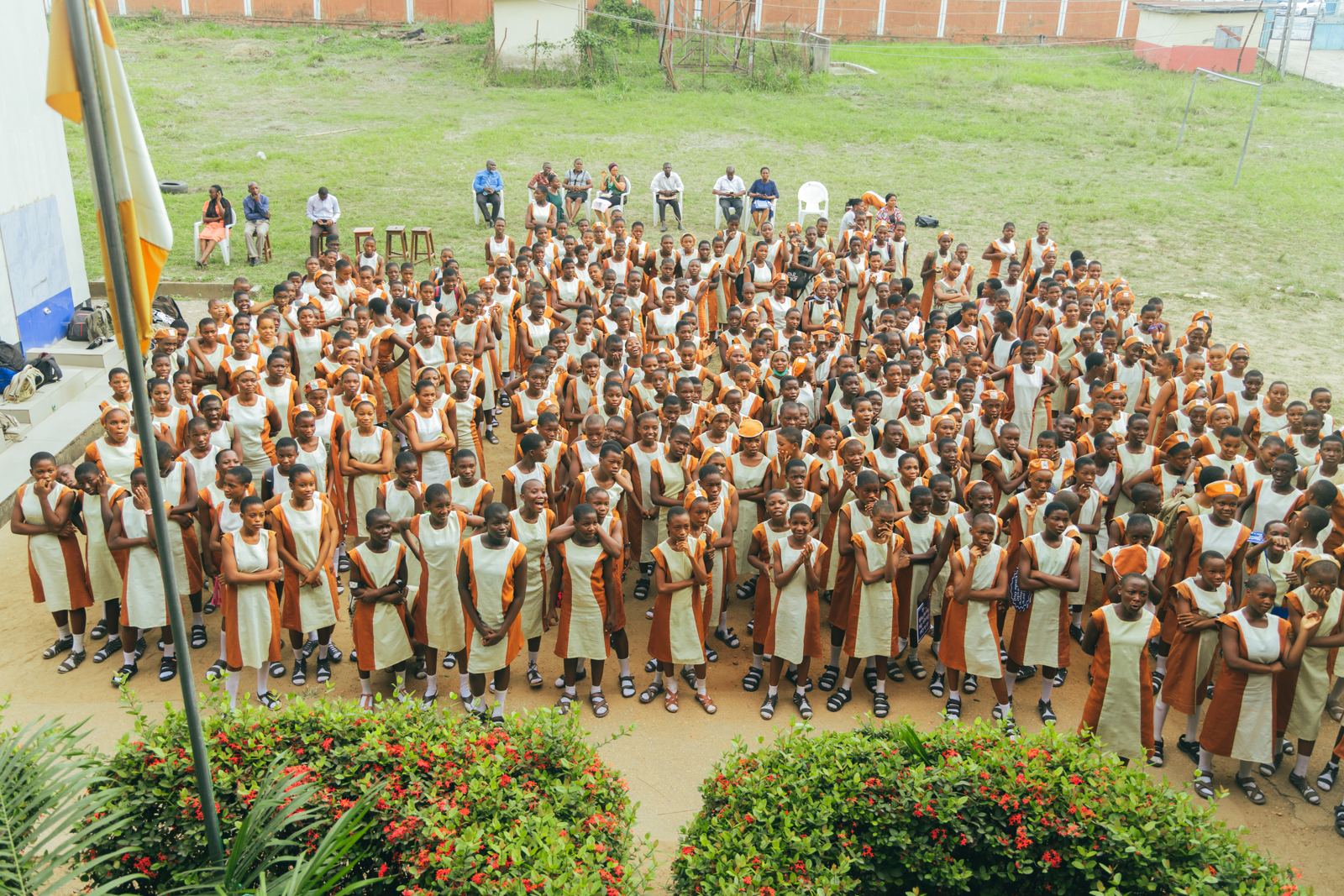 A large assembly of students in orange and cream uniforms gathered on a school field
