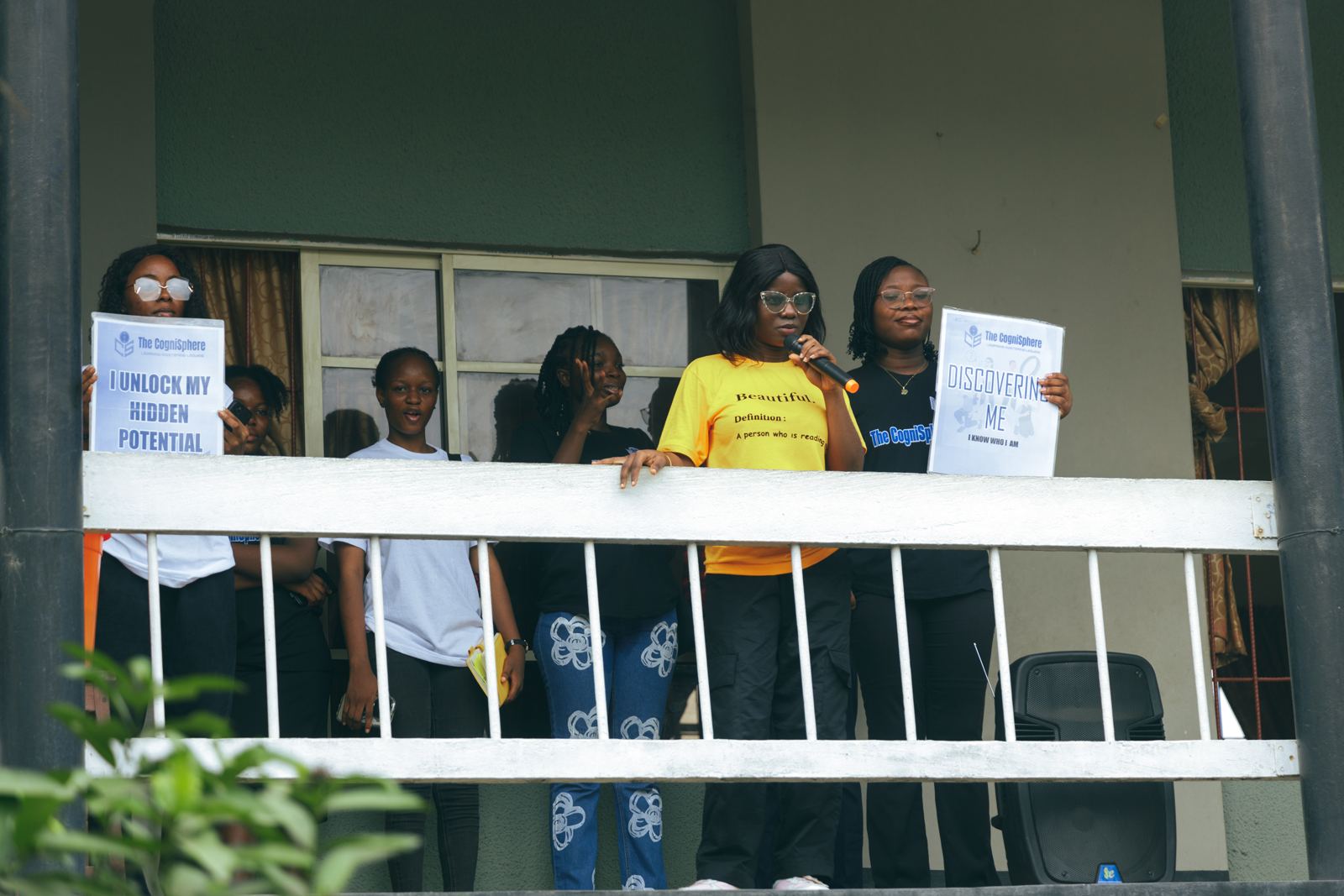 Volunteers on a school balcony holding signs reading "I unlock my hidden potential" and "Discovering Me"
