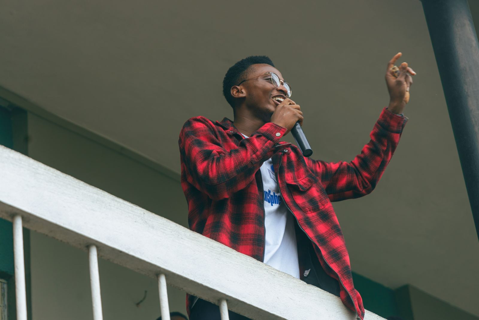 A young speaker in a red plaid shirt speaks into a microphone with one arm raised